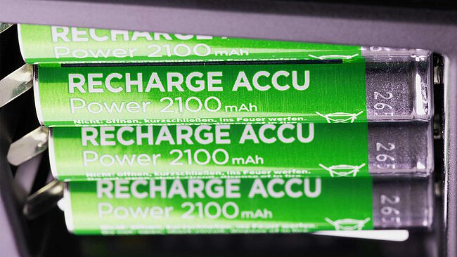 four metallic-green shining rechargeable batteries of standard size AAA with the imprint RECHARGE ACCU close-up in a black battery charger