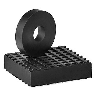 a black, square rubber board made of elastomer NBR with small square indentions on the surface as non-slip protection, on top of which stands an upright black, round rubber disc without surface profiling and a centered hole, isolated on white background 