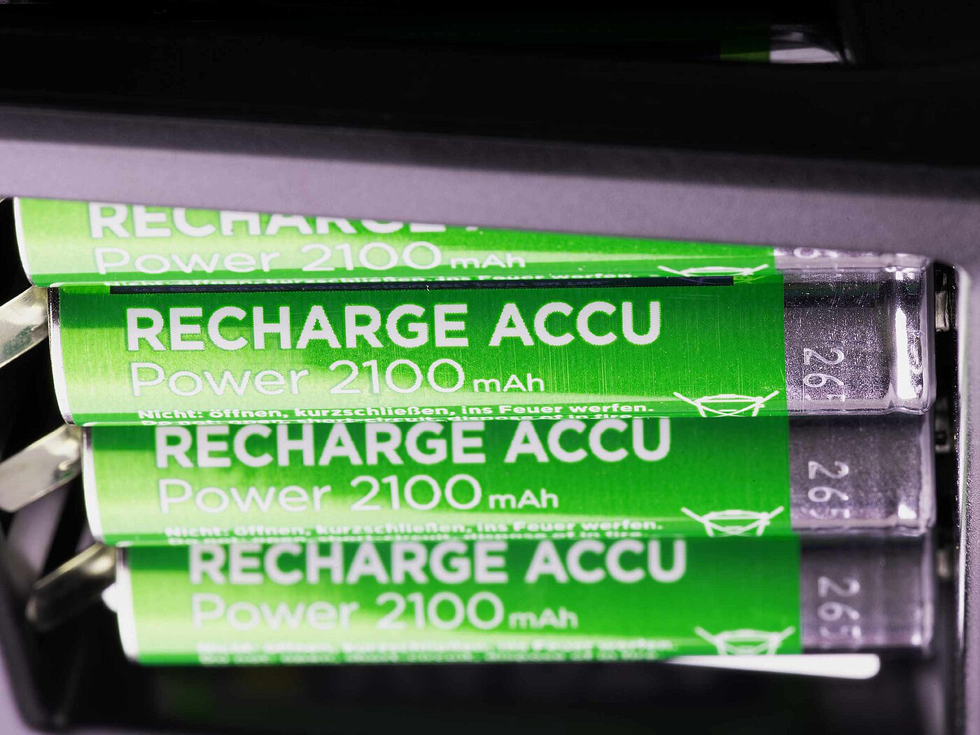 four metallic-green shining rechargeable batteries of standard size AAA with the imprint RECHARGE ACCU close-up in a black battery charger